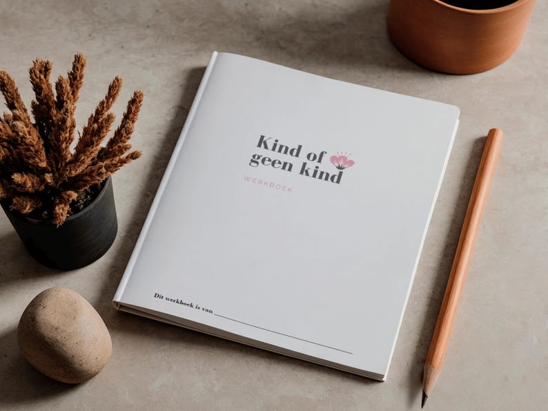 May include: A white workbook with the text "Kind of geen kind" and a floral design. A pencil, a small potted plant, and a decorative stone are next to the book. The workbook is on a neutral surface.