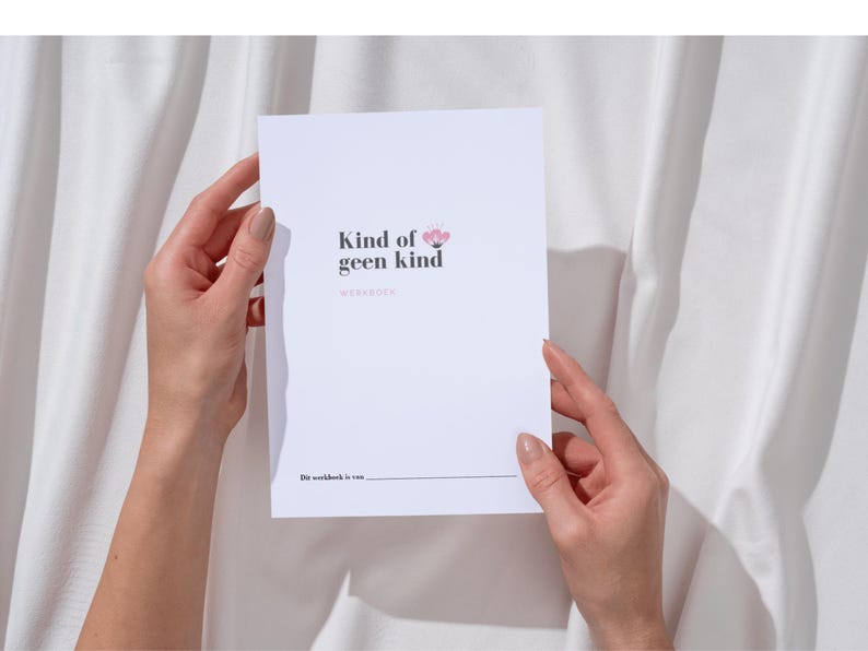 May include: A white workbook with the text "Kind of geen kind" and a floral design is held by two hands. The workbook's title is in a dark font, with the word "workbook" below. The background is a white fabric.
