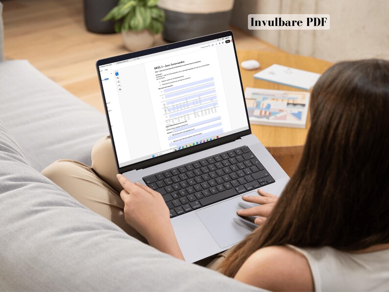 May include: A laptop displaying a document titled "Invulbare PDF" is open on a person's lap. The laptop has a black keyboard and a silver frame. The person is sitting on a gray couch.