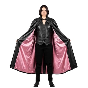 May include: A black leather cape with a pink satin lining. The cape is open, revealing a black leather vest and black pants. The model is standing against a white background.