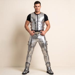May include: A metallic silver vest with a front zip and side buckles, paired with matching silver trousers featuring reinforced knee panels and side buckles, worn over a black short-sleeved shirt with silver boots featuring multiple straps.