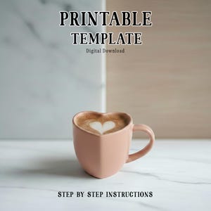 Op de afbeelding: Een roze hartvormige mok gevuld met koffie, met een hartvormig schuimontwerp. De afbeelding bevat de tekst "PRINTABLE TEMPLATE" en "STEP BY STEP INSTRUCTIONS". De achtergrond is een marmeren oppervlak.
