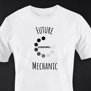 Könnte beinhalten: Weißes T-Shirt mit dem schwarzen Schriftzug "FUTURE MECHANIC" und einem Ladekreis-Grafik. Die Grafik wechselt von Schwarz zu Grau. Ein lässiges Kleidungsstück für den Alltag.