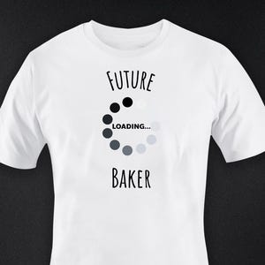 Könnte beinhalten: Weißes T-Shirt mit dem schwarzen Schriftzug "FUTURE BAKER" und einem Ladesymbol. Das Ladesymbol ist eine Reihe von schwarzen und grauen Kreisen. Das T-Shirt hat kurze Ärmel und einen Rundhalsausschnitt.