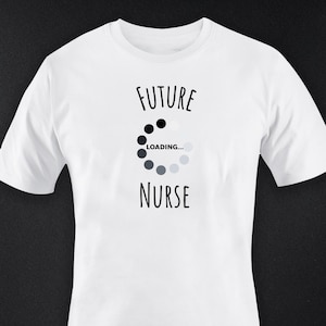 Könnte beinhalten: Weißes T-Shirt mit dem Text "FUTURE NURSE" über und unter einem Ladekreis-Grafik. Der Ladekreis besteht aus schwarzen und grauen Punkten. Das Shirt hat einen Rundhalsausschnitt und kurze Ärmel.