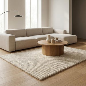 K&ouml;nnte beinhalten: Ein modernes Wohnzimmer mit einem hellbeigen Ecksofa, einem runden Couchtisch aus Holz und einem cremefarbenen Teppich. Eine schwarze Bogen-Stehleuchte und dekorative Vasen erg&auml;nzen das minimalistische Design. Der Raum hat Holzb&ouml;den und gro&szlig;e Fenster.