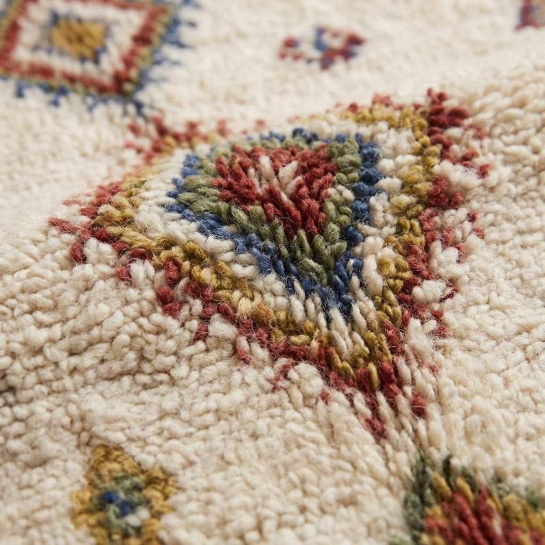 Close-up of handwoven Moroccan wool rug showing thick plush texture, looped fibers, and colorful geometric detailing in red, blue, and mustard tones