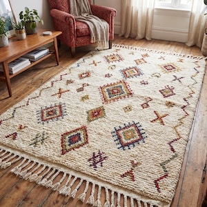 Ivory Moroccan boho rug with colorful geometric pattern styled in a cozy living room with wooden floor and armchair, showcasing soft wool texture and fringe detail