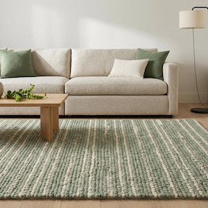 May include: A living room setting with a neutral-toned sofa and green and cream cushions. A striped rug in green and white is on the floor. A wooden coffee table and a floor lamp are also visible.