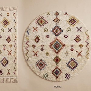 May include: Three ivory-colored rugs with geometric patterns. The rugs are rectangular, round, and runner-shaped. Each rug features diamond and cross designs in shades of red, blue, green, and brown. The rectangular and runner rugs have fringed edges.
