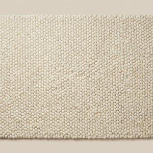 Top-down view of solid ivory textured wool rug with dense looped surface