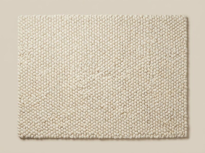 Top-down view of solid ivory textured wool rug with dense looped surface