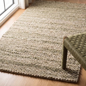 May include: A rectangular, textured rug in shades of beige and green. The rug has a nubby, woven appearance and is placed on a hardwood floor. A portion of a green woven bench is visible on the right side of the image.