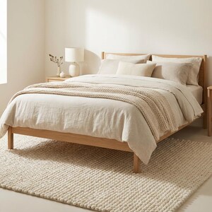 K&ouml;nnte beinhalten: Ein helles Holzbett mit einer beigen Bettdecke und Kissen. Eine beige Strickdecke liegt auf dem Bett. Zwei passende Nachttische mit Lampen flankieren das Bett. Ein cremefarbener Teppich liegt auf dem Boden.