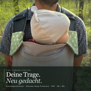 Könnte beinhalten: Eine Babytrage mit einem Baby, das einen hellgrauen Hut trägt. Die Trage hat grüne und weiße gepunktete Schultergurtschoner. Der Text "Deine Trage. Neu gedacht." ist sichtbar.