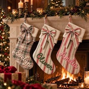 May include: Three Christmas stockings hanging from a mantelpiece. The first is plaid with the name Evelyn, the second is striped with the name Oliver, and the third is striped with the name Amelia. Each stocking features a large fabric bow.