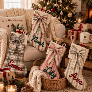 Peut inclure: Quatre chaussettes de Noël en tissu avec des motifs à carreaux et à rayures ornées de grands nœuds. Chaque chaussette est personnalisée avec les prénoms brodés Noah, Emma, Lily et Ava en écriture rouge ou verte dans un décor festif.