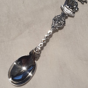 Peut inclure: Une cuillère en argent avec un manche orné et un élément décoratif détaillé en haut. Le bol de la cuillère est de forme ovale et reflète l'environnement. Le manche a un design torsadé au milieu.
