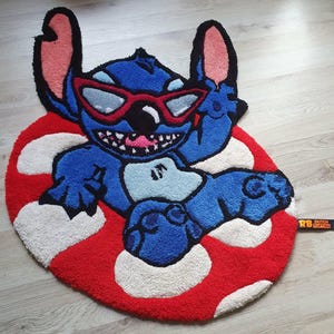 Könnte beinhalten: Blauer Teppich mit einer Cartoonfigur mit Sonnenbrille, die auf einem rot-weißen Pilzdesign liegt. Der Teppich besteht aus einem weichen, strukturierten Material. Die Figur hat ein breites Grinsen.