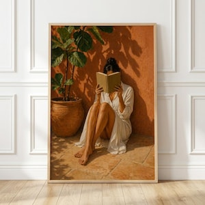 Pode incluir: Uma impressão de arte de parede emoldurada retratando uma pessoa com um vestido branco sentada num chão cor de terracota, segurando um livro aberto à frente do rosto. Uma grande planta verde em vaso à esquerda projeta sombras numa parede laranja.