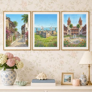 Peut inclure: Trois impressions aquarelles encadrées alignées. L'image de gauche montre une rue pavée avec des bâtiments en pierre et des fleurs. Celle du centre représente un fort en pierre au bord de la mer avec deux voiliers. Celle de droite montre une cour.