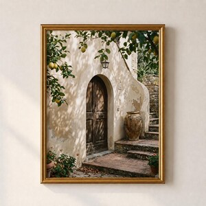 May include: A framed wall art print depicting a Mediterranean-style building with a beige stucco facade, a dark wooden arched door, and a large terracotta urn on stone steps. A lemon tree with yellow fruit hangs over the entrance area.