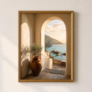 May include: A framed wall art print featuring a stone archway overlooking a coastal landscape with a sea view. A large brown terracotta pot containing a small green olive tree sits on the stone floor, casting a shadow against the wall.