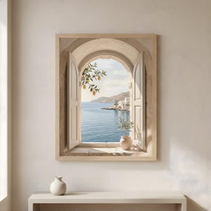 May include: A framed print showing an open window with a coastal view. The window, with open shutters, reveals a blue sea, white buildings, and a lemon tree. A small vase with a plant sits on the windowsill. The frame and window are light beige.