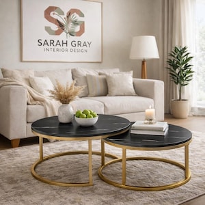 Puede incluir: Dos mesas de centro redondas con tapas de mármol negro y bases de metal dorado. Las mesas están anidadas, una ligeramente más pequeña que la otra. La mesa más grande tiene un jarrón con flores secas y un cuenco con fruta verde. La mesa más pequeña tiene una vela.