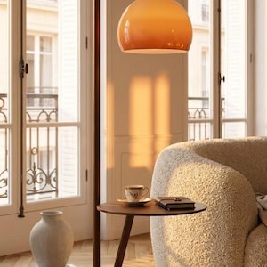 May include: A modern floor lamp with a warm orange glass shade and a dark brown metal frame. The lamp has a built-in side table with a small cup and books. The lamp is 72 inches tall.