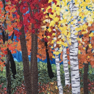 May include: A close-up of a fabric art piece depicting a forest scene with trees in various shades of red, yellow, and green. The trees are made of fabric scraps and are sewn together to create a textured effect.