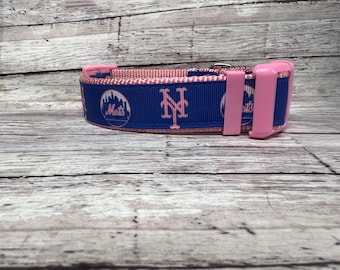 May include: A blue and pink dog collar featuring the New York Mets logo and team name. The collar has a pink interior and pink plastic hardware. The Mets logo is in white and the team name is in pink.