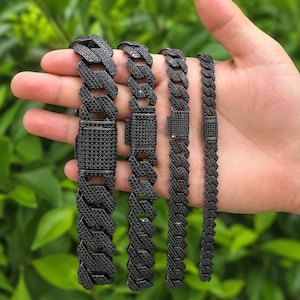 May include: Four black metal cuban link bracelets of varying widths, each featuring a rectangular box clasp closure. The surface of every link and the clasp on each bracelet is densely covered in small, dark, reflective stones.
