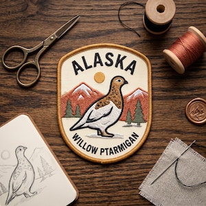 May include: An embroidered patch featuring a Willow Ptarmigan bird, mountains, and trees with the text ALASKA and WILLOW PTARMIGAN. The patch has a cream background, a mustard yellow border, and is surrounded by sewing tools including scissors and thread.