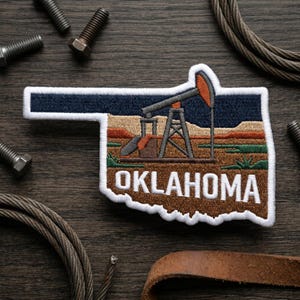 May include: Embroidered patch in the shape of Oklahoma, featuring a dark blue sky, a brown and orange oil derrick, and the word "OKLAHOMA" in white. The patch has a white border and a brown, tan, and green landscape.