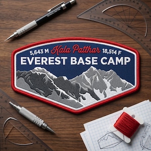 May include: Embroidered patch with the text "EVEREST BASE CAMP" and "Kala Patthar 5,643 M 18,514 F" in red and white on a blue background, with a mountain range design. The patch is surrounded by a red border. The image also includes drafting tools and a spool of red thread.
