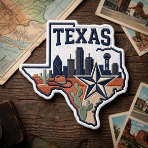 May include: Embroidered patch in the shape of Texas, featuring a skyline, a star, a cowboy hat, and cacti. The word "TEXAS" is embroidered in navy blue. The patch is bordered in white and set against a wooden background.