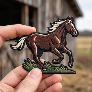 May include: An embroidered patch featuring a brown horse with a white mane and tail, depicted in a running pose over a patch of green grass. The design is outlined in black thread, showcasing detailed stitching of the horse's muscular form.