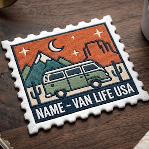 May include: Embroidered patch with a retro van design, mountains, and cacti under a night sky. The patch reads "NAME - VAN LIFE USA" in a blue border. A compass, keys, and a mug are in the background.