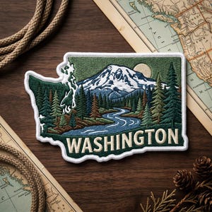 May include: Embroidered patch in the shape of Washington state, featuring a mountain landscape with a river and trees. The word "WASHINGTON" is displayed in white block letters. The patch is bordered in white.