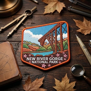 May include: A rectangular embroidered patch featuring the New River Gorge National Park bridge in brown, blue, and green. The text NEW RIVER GORGE NATIONAL PARK is stitched in white at the bottom, accented by small pink flowers on a dark brown background.