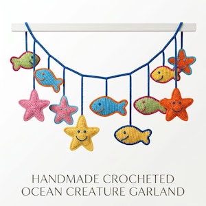 Puede incluir: Una guirnalda de criaturas marinas hechas a mano con ganchillo, con coloridos peces y estrellas de mar. La guirnalda está suspendida de una barra blanca con hilo azul. Los peces son azules, amarillos y verdes, y las estrellas de mar son rosas, naranjas y amarillas.
