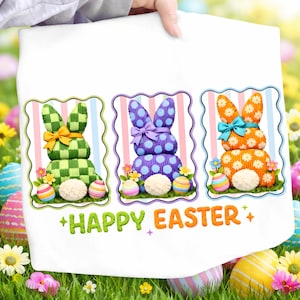 Könnte beinhalten: Weißes Ostertuch mit drei dekorativen Hasen-Designs in Grün, Lila und Orange. Jeder Hase hat einen flauschigen Schwanz, eine Schleife und ist von Blumen und Ostereiern umgeben. Der Text "HAPPY EASTER" ist in Grün und Orange gedruckt.