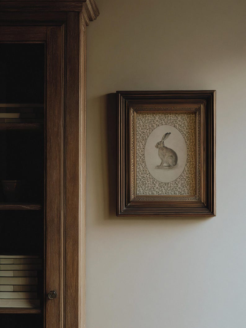 Hare wall art displayed on a narrow wall near a bookcase, evoking a quiet interior setting.