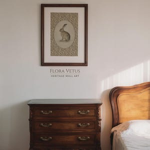 Framed hare artwork above a wooden dresser in a softly lit bedroom with a country house atmosphere.