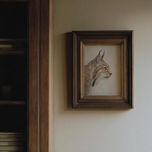 Small framed bobcat print on a darker wall in low light, cabinet-like study atmosphere.
