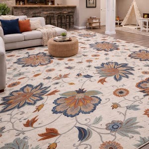 Puede incluir: Una gran alfombra con fondo crema y un patrón floral en tonos azules, naranjas y verdes. La alfombra está en un salón con un sofá, un otomán y una zona de bar.