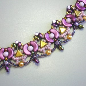 Op de afbeelding: Een close-up van een kralenketting met een geometrisch ontwerp. De ketting is gemaakt met paarse, roze, gouden en groene kralen.