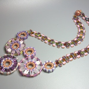 May include: A multi-strand necklace with a geometric design featuring multiple circles of pink, purple, and white beads. The necklace is made with seed beads and has a copper clasp.