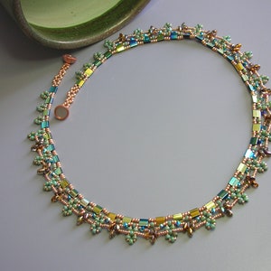 May include: A beaded necklace with a magnetic clasp. The necklace features a repeating pattern of small, iridescent green, blue, and gold beads. The necklace is accented with small clusters of green beads and brown beads.